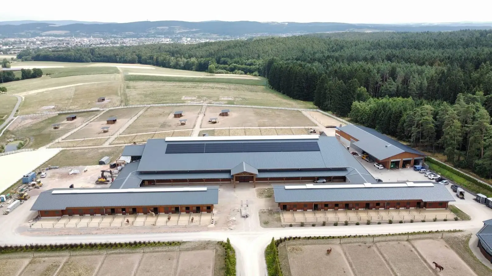 Reitanlage mit Photovoltaik auf dem Hallendach, dahinter Wald
