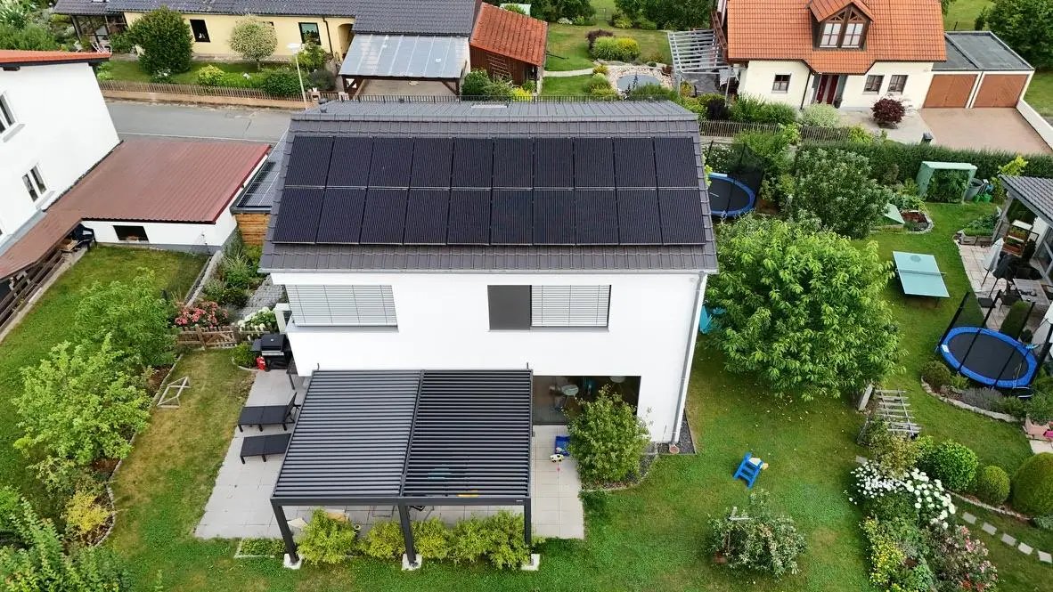 Wohnhaus mit schwarzen Modulen auf dem Satteldach, Luftaufnahme
