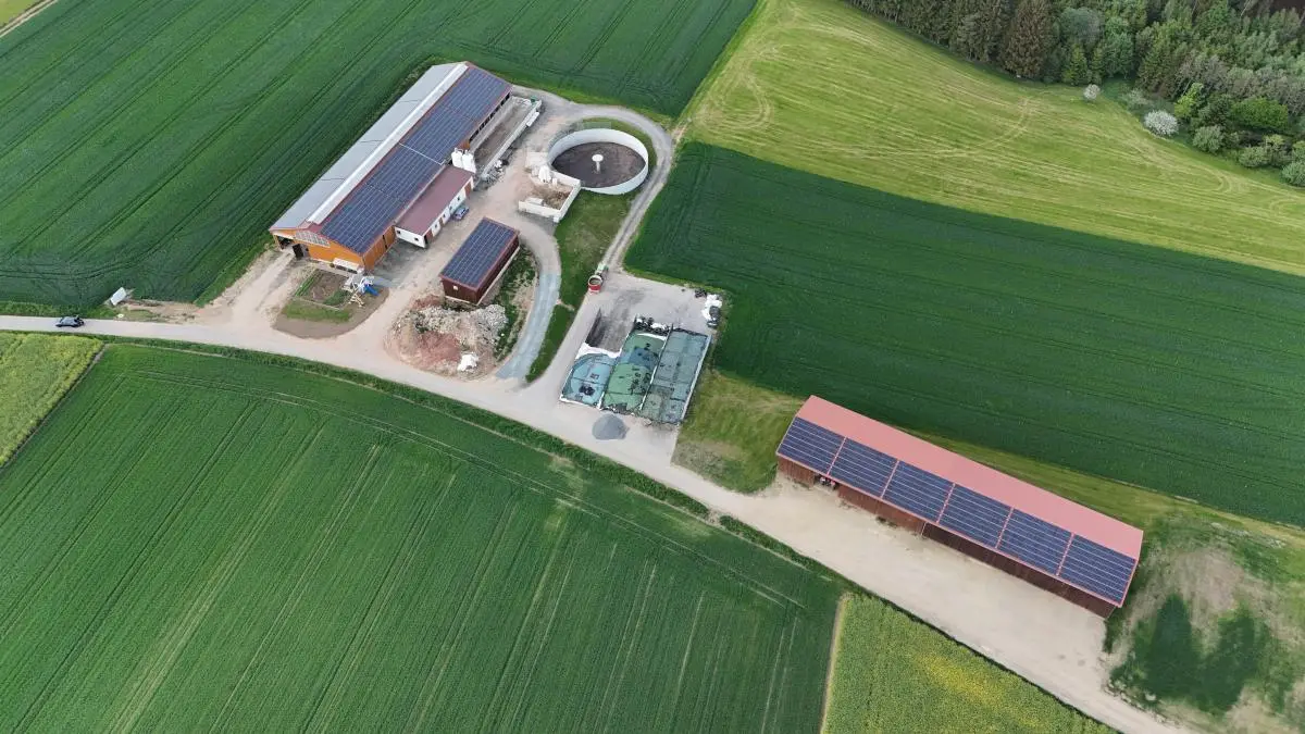 Luftaufnahme eines Hofs zwischen Feldern, Photovoltaik auf mehreren Dächern